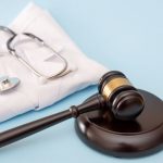 Stethoscope on folded doctor's lab coat and Gavel on Blue Background for Healthcare Law Concepts