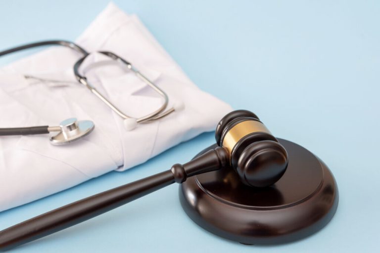 Stethoscope on folded doctor's lab coat and Gavel on Blue Background for Healthcare Law Concepts